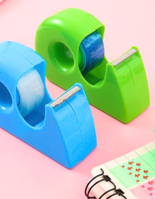 Blue and green tape dispensers with rolls of adhesive tape on a pink background.